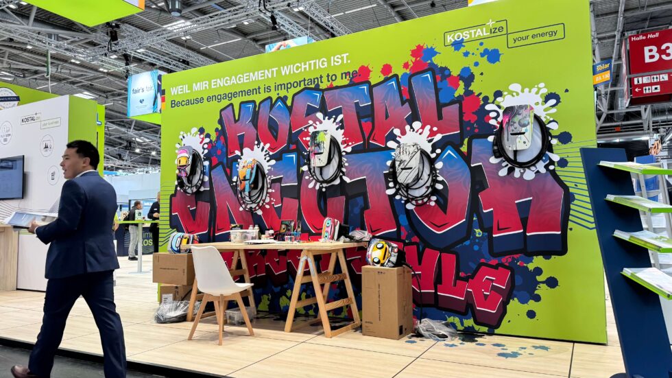 Kostal Enector Messestand mit Besucher davor und die Graffiti-Wallbox für die Stille-Auktion in München.